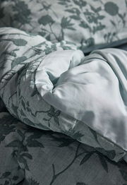 Nahaufnahme von Bettwäsche mit floralem Muster in sanften Grüntönen, perspektivisch von der Seite aufgenommen.