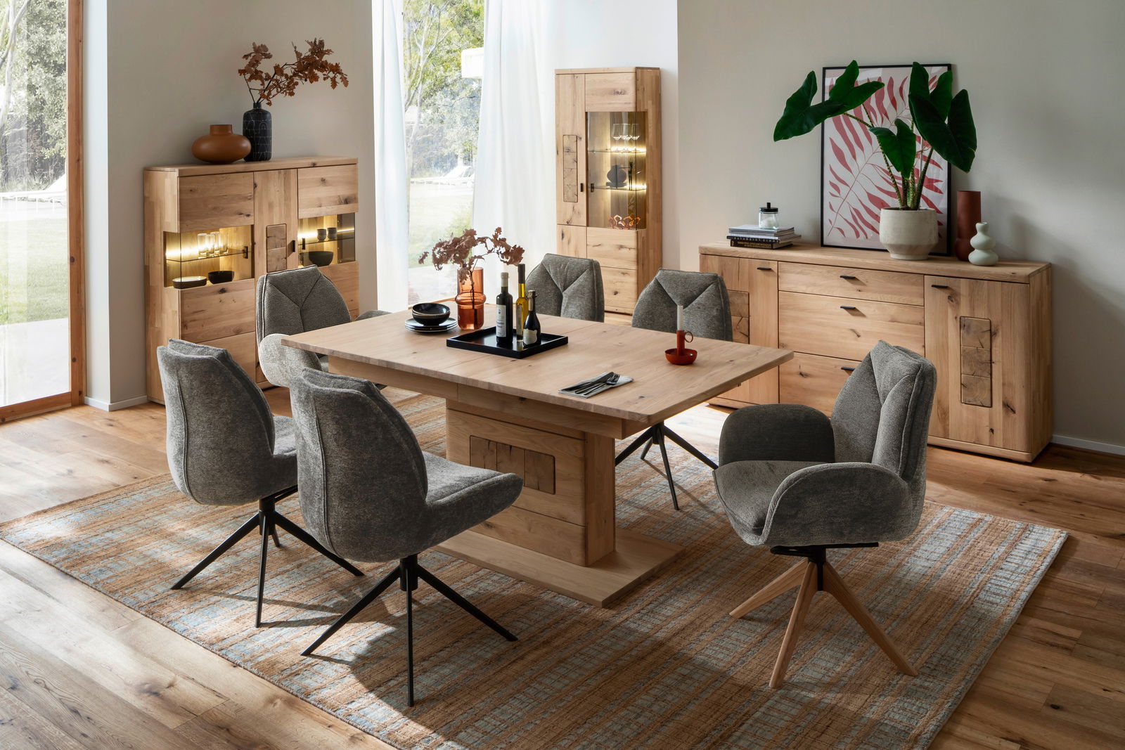 Linea Natura Vitrine PHÖNIX Esszimmer mit Holztisch und grauen Stühlen, umgeben von Vitrinen und Sideboards aus Holz, aus der Perspektive des Raumes betrachtet.