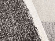 Nahaufnahme eines mehrfarbigen Teppichs mit grauen und cremefarbenen Bereichen, perspektivisch von oben fotografiert.