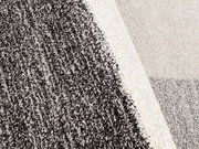 Nahaufnahme eines mehrfarbigen Teppichs mit grauen und cremefarbenen Bereichen, perspektivisch von oben fotografiert.