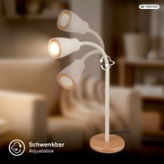Weiße Stehleuchte mit drei schwenkbaren Spot-Köpfen und goldfarbenem Standfuß, warm leuchtend, in schräger Vorderansicht vor unscharfem Wohnzimmerhintergrund