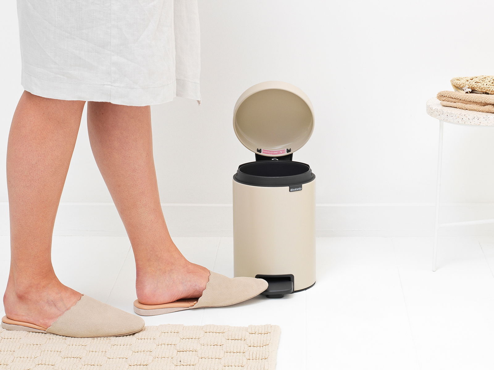 Beige Treteimer 3L mit geöffnetem Deckel, seitliche Perspektive, neben einer Person in Hausschuhen.
