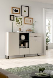 Modernes Sideboard in Cremeweiß mit schwarzen Metallfüßen, mittigem offenem Regal und drei Schubladen rechts, in einem hellen Wohnzimmer dekoriert; Perspektive: frontale Ansicht leicht von links
