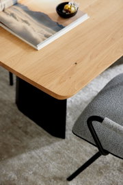 Schreibtisch mit heller Holzplatte und schwarzem Gestell, darauf ein Bildband und eine kleine Schale; Ansicht schräg von oben mit Fokus auf die Tischkante.