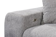 Nahaufnahme einer grauen Sofaecke mit strukturiertem Stoff und einem Metallknopf an der Seite, Perspektive von der Seite.