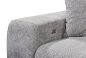 Nahaufnahme einer grauen Sofaecke mit strukturiertem Stoff und einem Metallknopf an der Seite, Perspektive von der Seite.