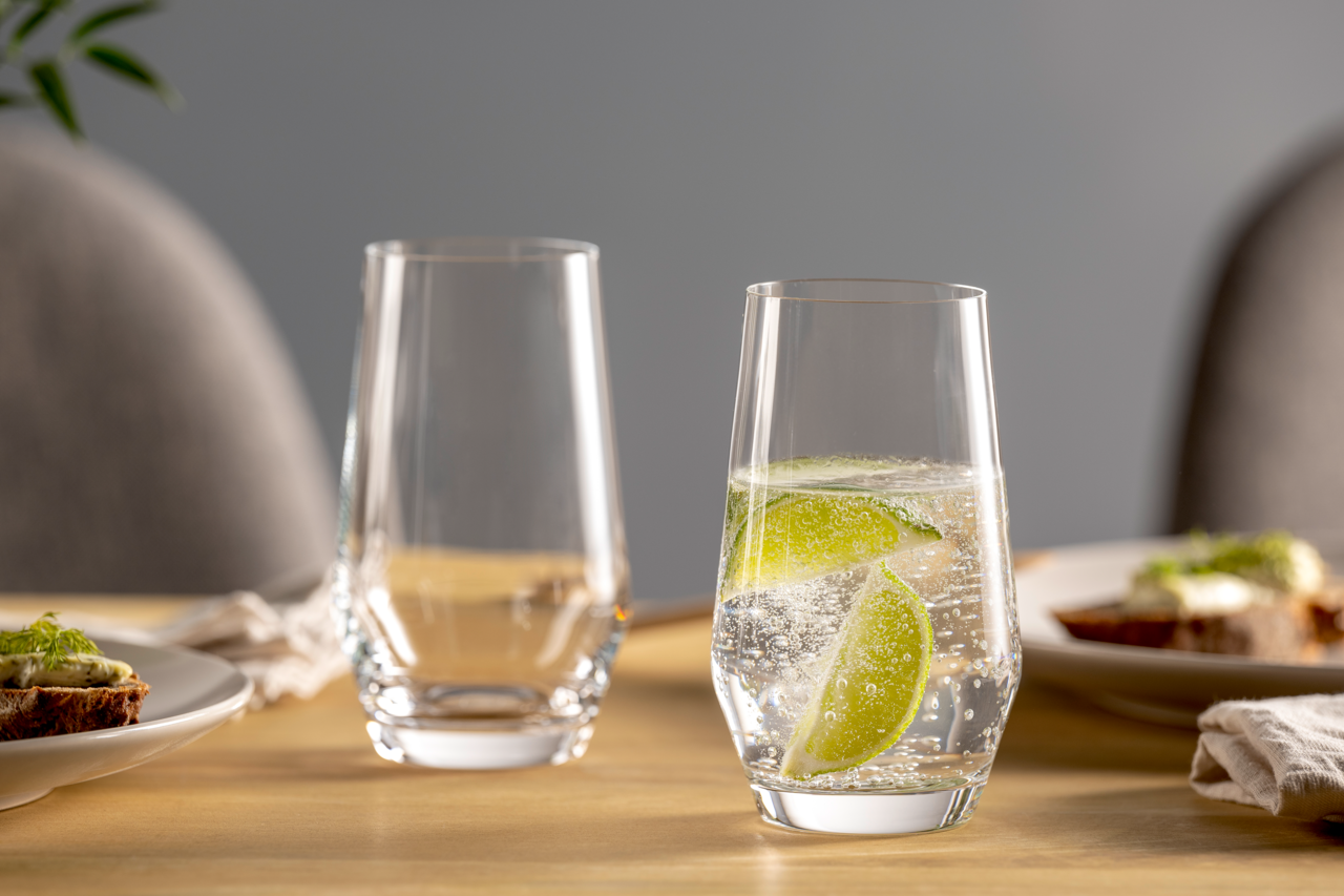 Zwei elegante Gläser auf einem gedeckten Tisch, eines gefüllt mit sprudelndem Wasser und Limettenscheiben, aus seitlicher Perspektive fotografiert.