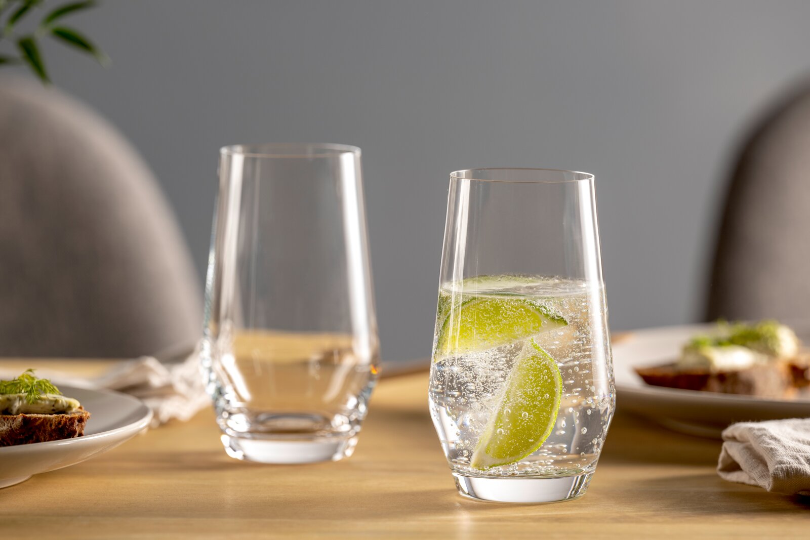 Leonardo Becher 6er-Set PUCCINI Zwei elegante Gläser auf einem gedeckten Tisch, eines gefüllt mit sprudelndem Wasser und Limettenscheiben, aus seitlicher Perspektive fotografiert.