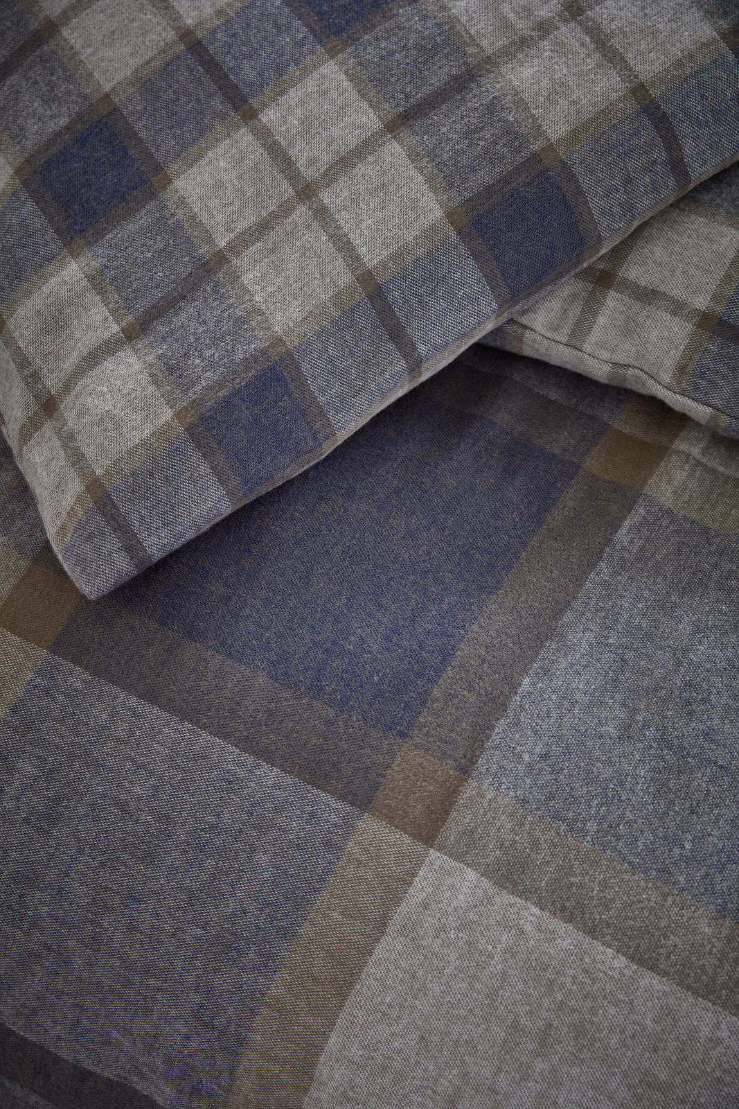 Nahaufnahme von kariertem Bettwäsche-Set in Blau- und Brauntönen, perspektivisch von oben fotografiert.