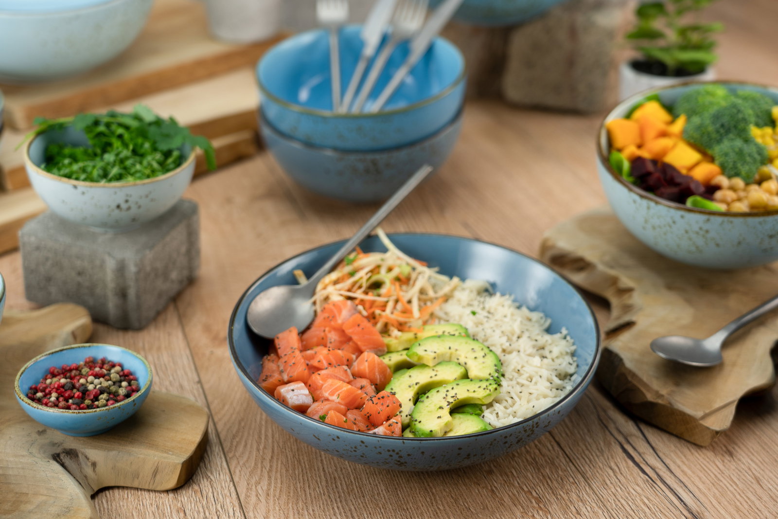 Poke Bowl Set aus vier Teilen in blauer Keramik, gefüllt mit frischen Zutaten wie Lachs, Avocado und Reis, aus der Vogelperspektive fotografiert.