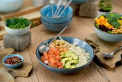 Poke Bowl Set aus vier Teilen in blauer Keramik, gefüllt mit frischen Zutaten wie Lachs, Avocado und Reis, aus der Vogelperspektive fotografiert.