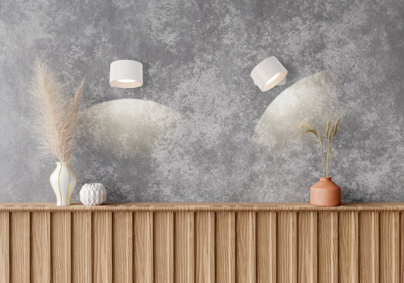 Zwei weiße, zylindrische Wandspots an grauer Strukturwand, die warmes Licht nach unten werfen Frontansicht der Wand mit leicht schräger Perspektive auf die rechte Leuchte über Holzsideboard mit Deko-Vasen.