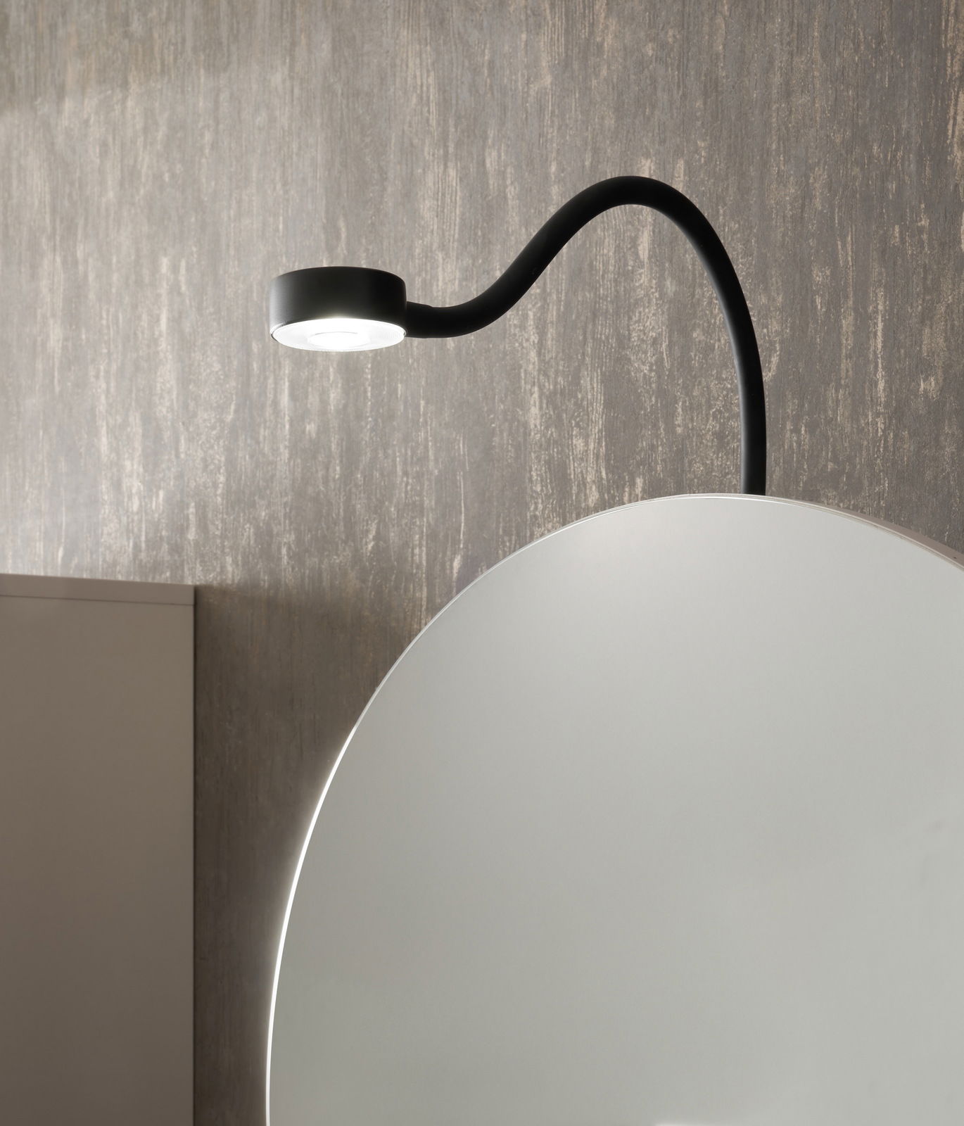 Nahaufnahme eines Spiegelschranks mit runder Spiegeloberfläche und integrierter schwarzer LED-Leuchte von oben.