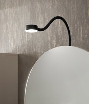 Nahaufnahme eines Spiegelschranks mit runder Spiegeloberfläche und integrierter schwarzer LED-Leuchte von oben.