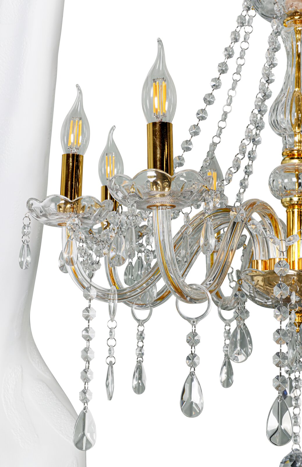 Detailaufnahme eines eleganten Kristall-Kronleuchters aus klarem Glas mit goldfarbenen Fassungen, geschwungenen Armen, Kristallketten und Tropfenanhängern, seitliche Nahansicht