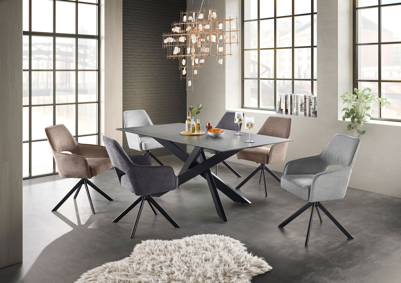 Set one by Musterring Esstisch BALTIMORE Moderner Esstisch mit schwarzer Tischplatte und X-förmigem Gestell, umgeben von sechs gepolsterten Stühlen in verschiedenen Farben, in einem hellen Raum mit großen Fenstern, aus der Perspektive von schräg vorne.