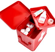 Rote Metall-Medizinbox mit geöffnetem Deckel, gefüllt mit Verbandsmaterial und Desinfektionsmittel, aus der Vogelperspektive fotografiert.