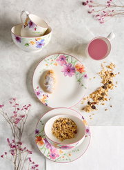 Frühstücks-Set mit floralem Design, bestehend aus Tassen, Schalen und Tellern, von oben fotografiert.