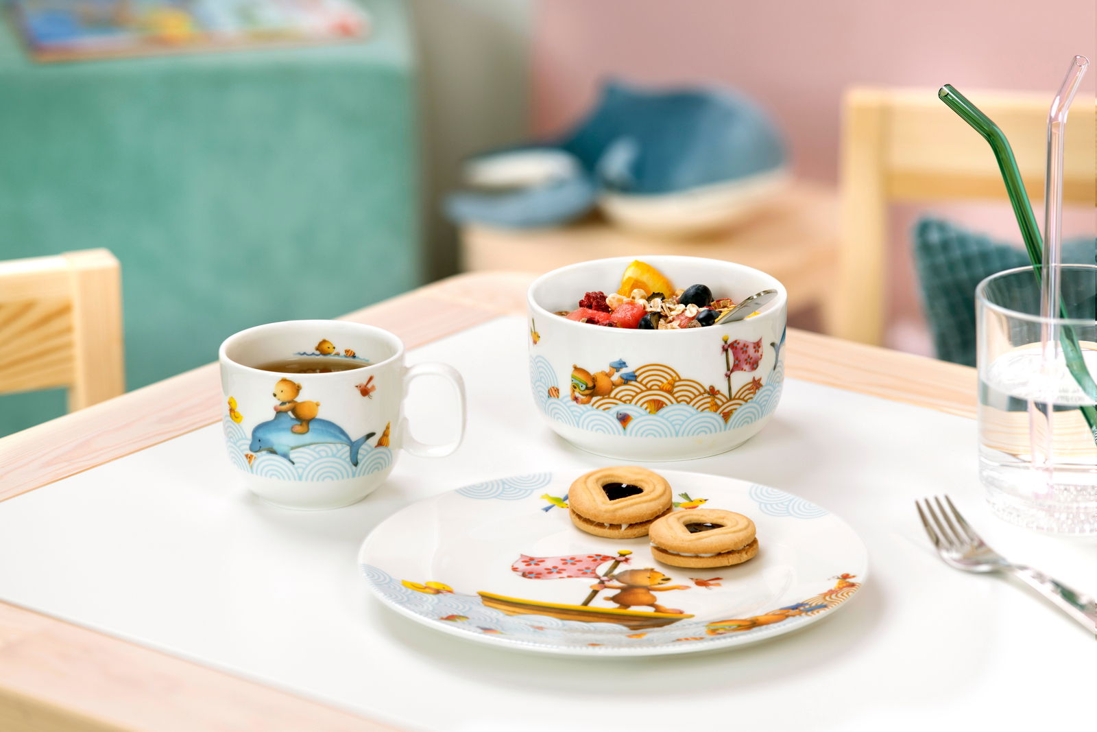 Kinder Geschirr-Set mit bunten Tiermotiven, bestehend aus Tasse, Schüssel und Teller, auf einem Tisch arrangiert. Perspektive von vorne.