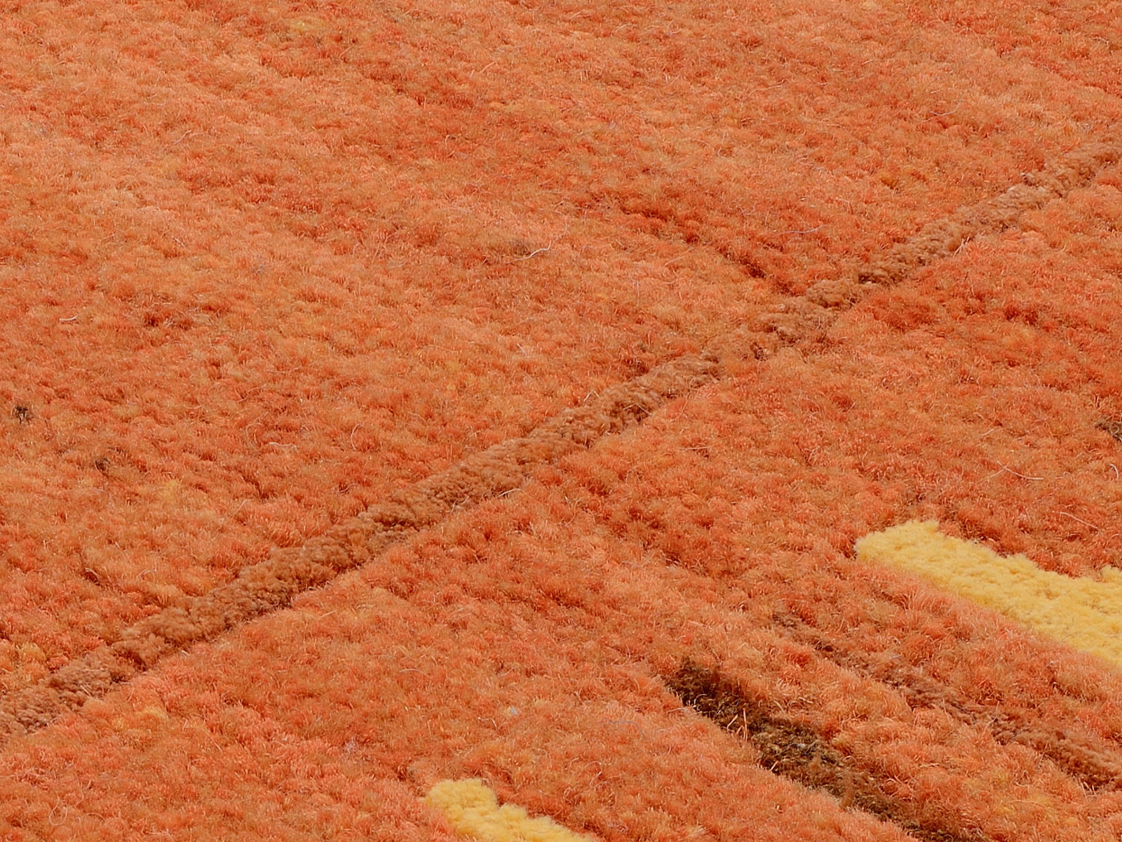 Nahaufnahme eines orangefarbenen Wollteppichs mit gelben Akzenten, aus der Vogelperspektive fotografiert.