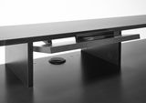 Nahaufnahme eines schwarzen Gaming-Schreibtisches mit erhöhtem Monitorständer und Kabeldurchführung, seitliche Perspektive.