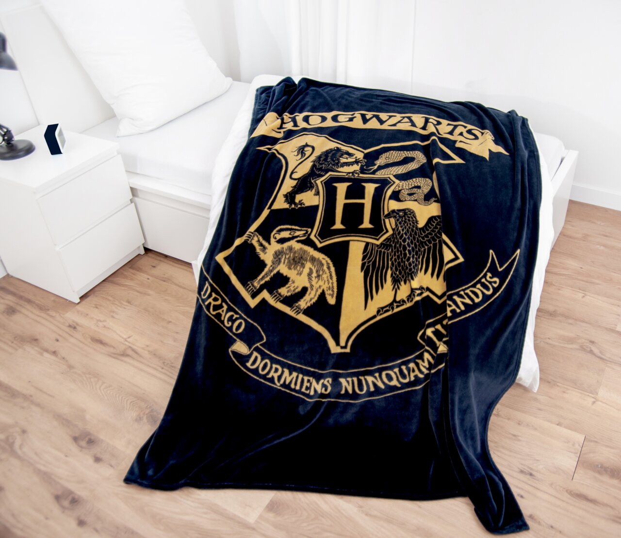 Harry Potter Wellsoft-Flauschdecke 150x200cm HARRY POTTER Weiche Wellsoft-Flauschdecke mit Hogwarts-Wappen, drapiert auf einem Bett in einem modernen Schlafzimmer.