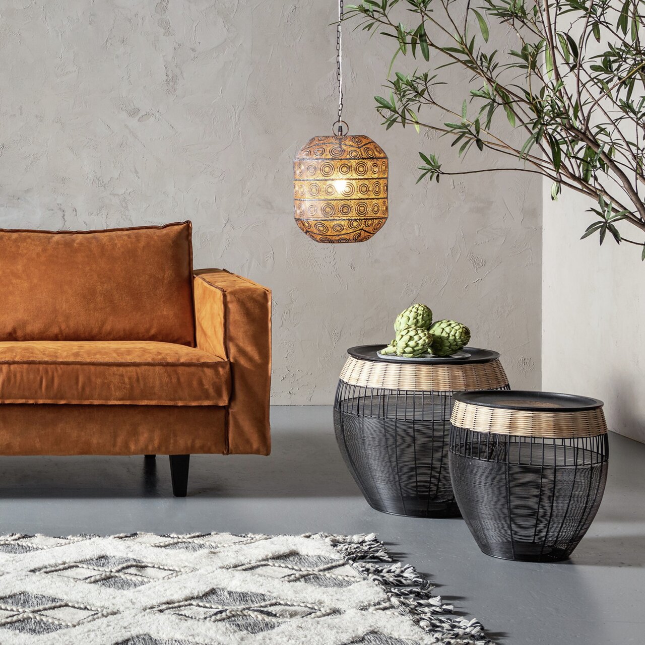 Set bijzettafels van zwart gaas met een rand van licht hout, in de woonkamer naast een bruine bank, gefotografeerd vanuit een zijdelingse hoek.