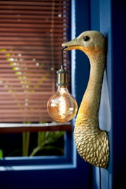 Goldene Wandleuchte in Form eines Vogels mit einer Glühbirne im Schnabel, seitliche Perspektive.