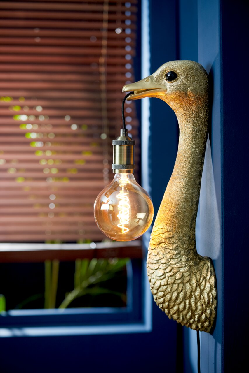 Goldene Wandleuchte in Form eines Vogels mit einer Glühbirne im Schnabel, seitliche Perspektive.