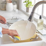 Eine Person reinigt eine gelbe Pfanne unter fließendem Wasser in der Küche. Die Perspektive zeigt die Pfanne von oben, während sie in der Spüle gehalten wird.