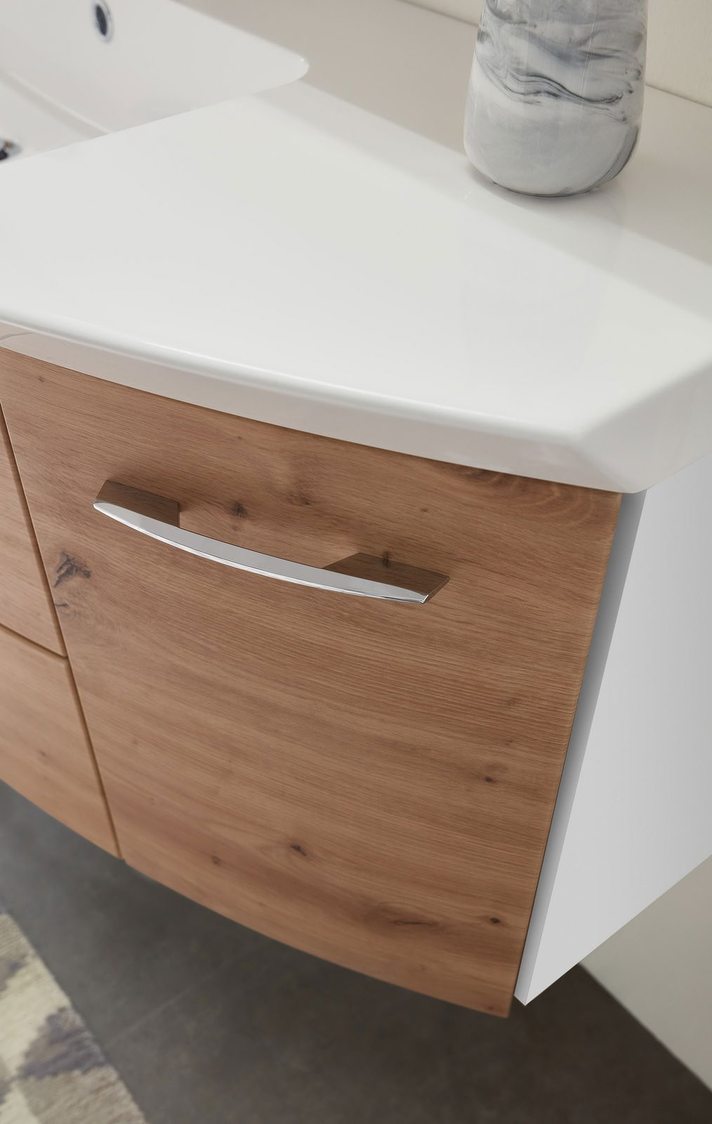 Nahaufnahme einer Badkombination mit Holzfront und weißer Waschtischplatte, seitliche Perspektive.