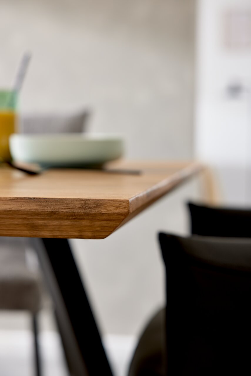 Nahaufnahme eines Esstisches mit Holzoberfläche und schwarzem Metallgestell, seitliche Perspektive.