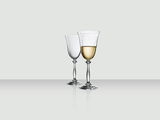 Zwei elegante Weingläser, eines gefüllt mit Weißwein, auf einer reflektierenden Oberfläche, seitliche Perspektive.