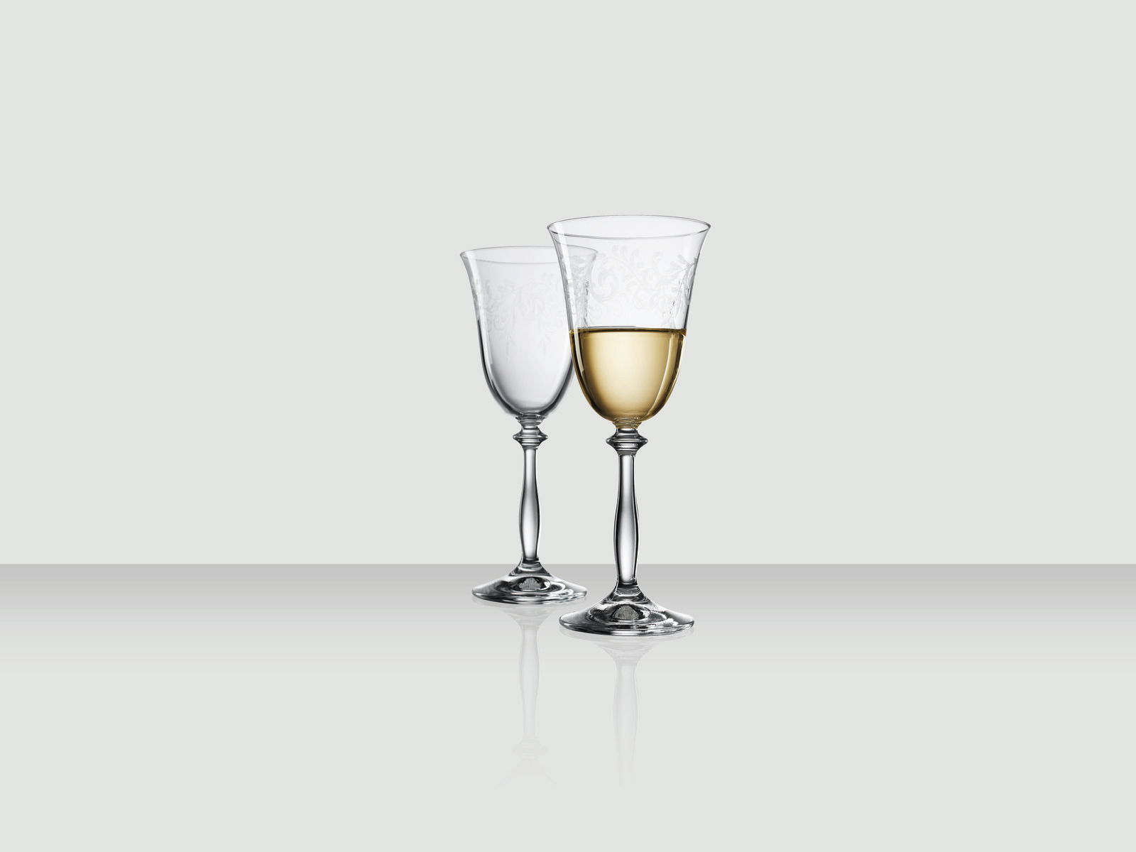 Zwei elegante Weingläser, eines gefüllt mit Weißwein, auf einer reflektierenden Oberfläche, seitliche Perspektive.