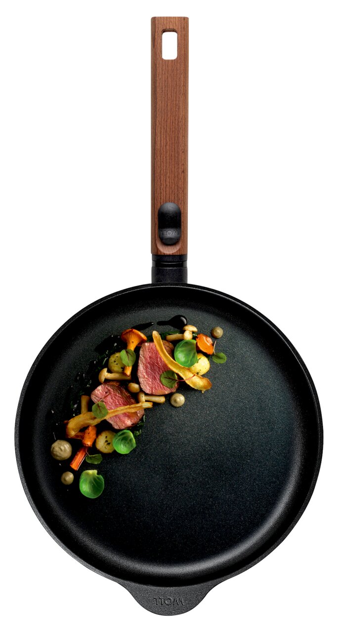 Gietijzeren koekenpan met houten handvat, gefotografeerd van bovenaf, met gebakken vlees en groenten.