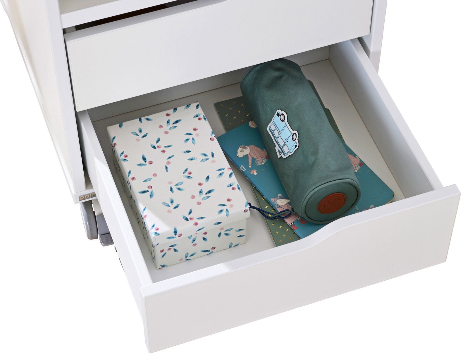 Offene Schublade eines weißen Rollcontainers mit Geschenkpapier und einer gerollten Decke, von oben betrachtet.