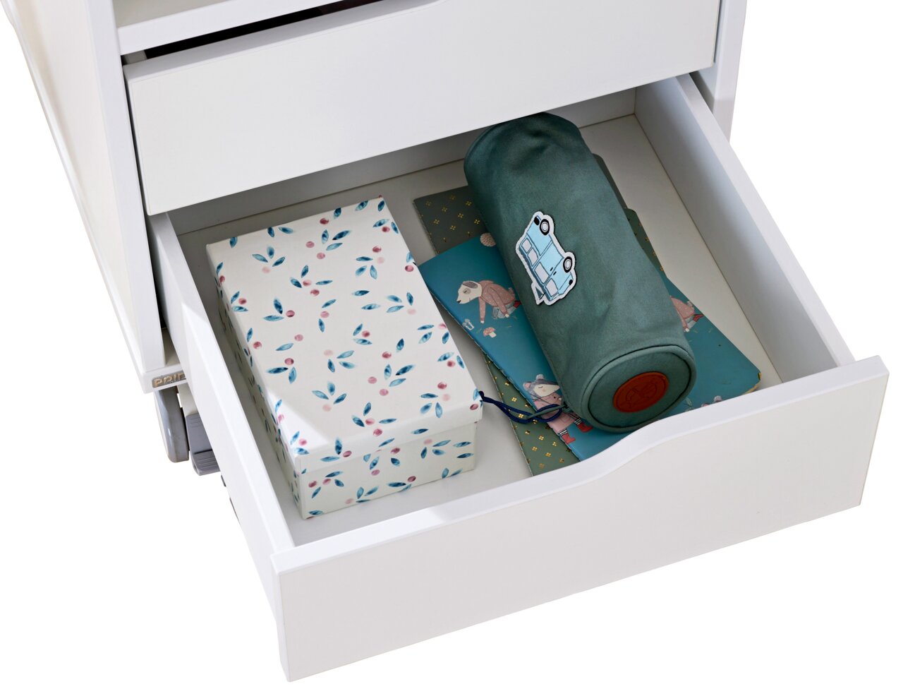Een open lade van een witte rolcontainer met cadeaupapier en een opgerolde deken, gezien van bovenaf.