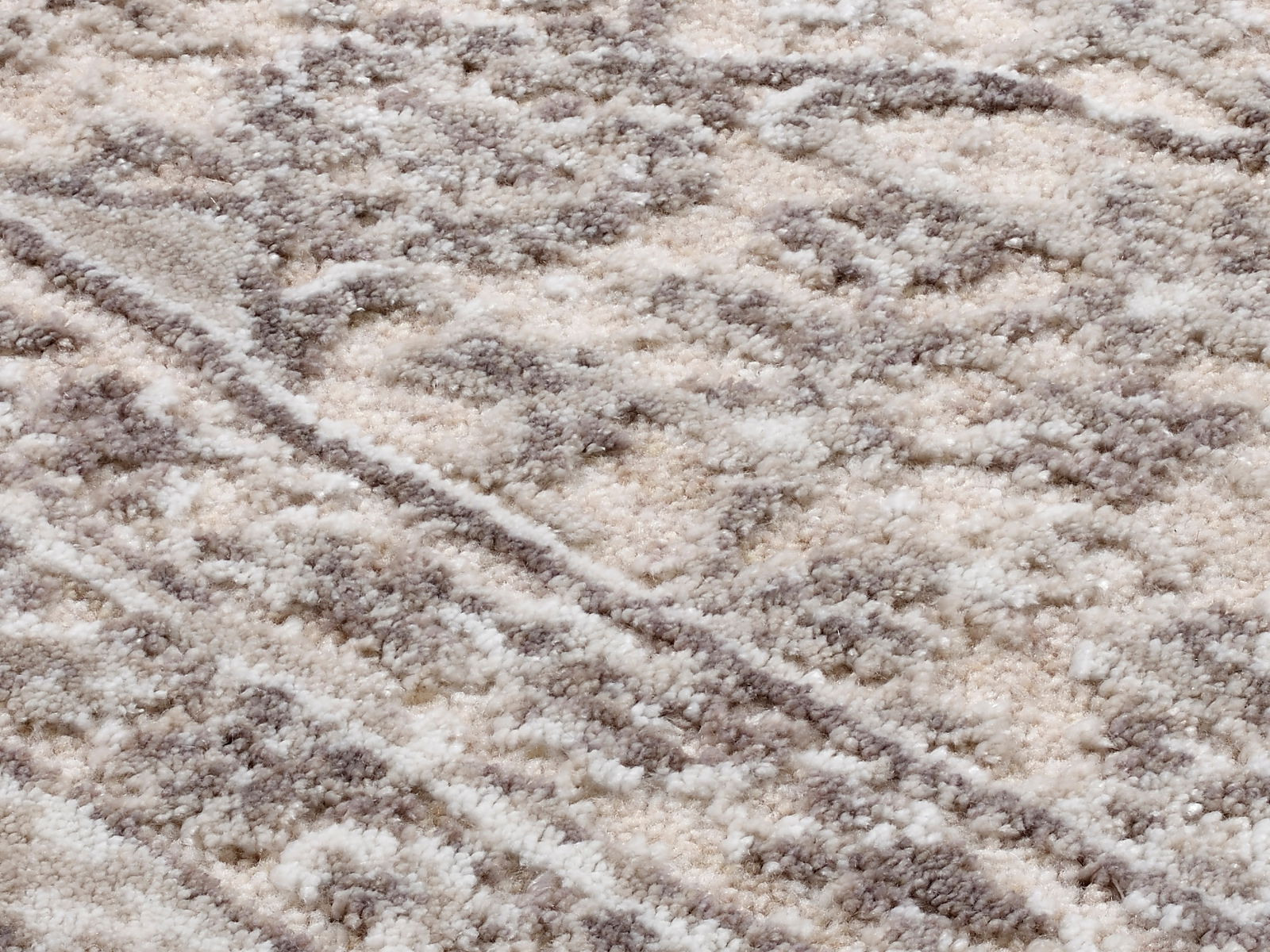Nahaufnahme eines Designer-Teppichs mit weicher, flauschiger Textur in creme- und grautönen, diagonale Perspektive.