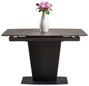 Moderner Esstisch mit dunklem Sockel und ausziehbarer Tischplatte, frontal betrachtet, dekoriert mit einer weißen Vase und rosa Blumen.