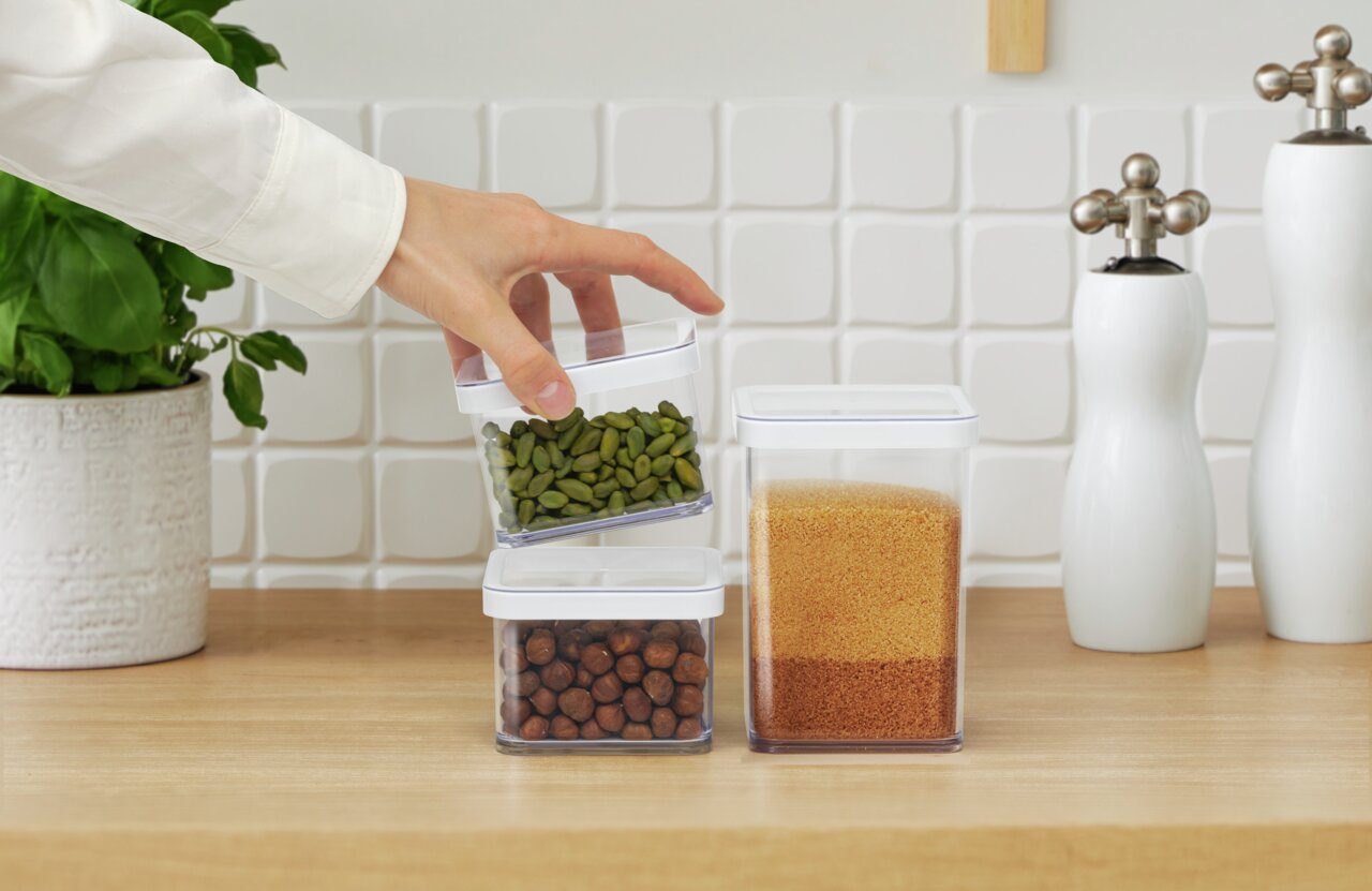 Quadratische Premium-Dose 0.5 l LOFT, gefüllt mit grünen Kernen, in der Hand gehalten, auf einer Küchenarbeitsplatte mit weiteren Dosen im Hintergrund.