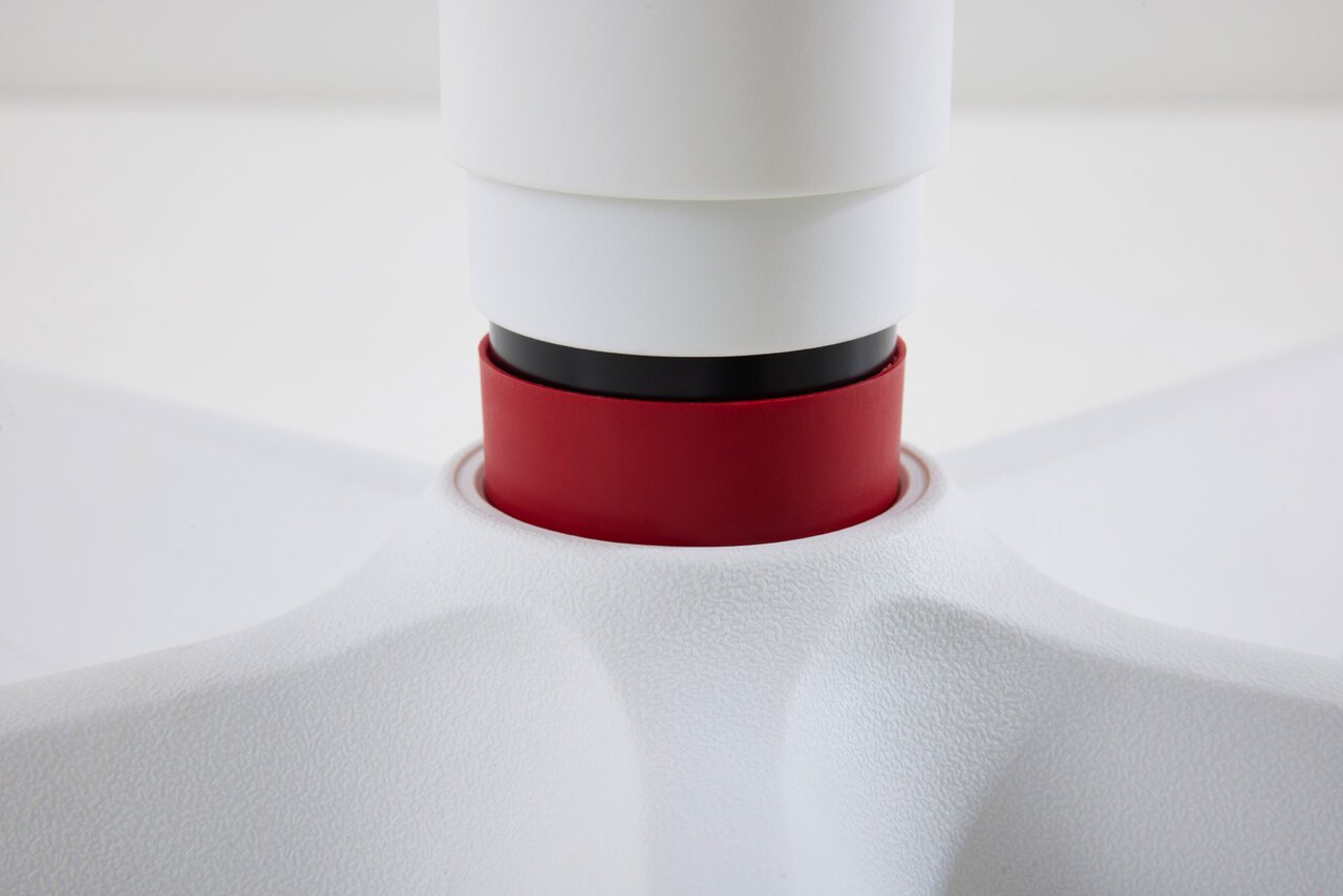 Close-up van een draaistoel voor jongeren in wit en rood, met de nadruk op de verbinding tussen zitting en onderstel.