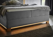 Boxspringbett in grauem Stoff mit Holzfüßen und integrierter Beleuchtung, seitliche Perspektive