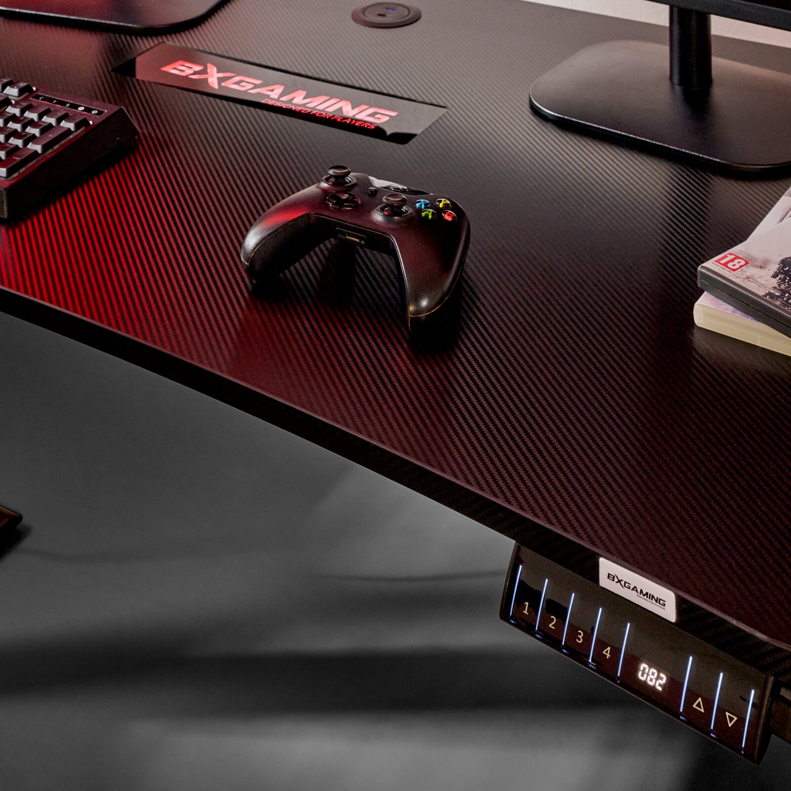 Gaming-Schreibtisch mit Carbon-Optik und BXGAMING-Logo, darauf ein schwarzer Gamecontroller; Ansicht schräg von oben (Top-Down-Perspektive) mit sichtbarem Bedienpanel an der Vorderkante.
