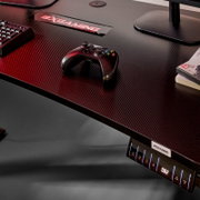 Gaming-Schreibtisch mit Carbon-Optik und BXGAMING-Logo, darauf ein schwarzer Gamecontroller; Ansicht schräg von oben (Top-Down-Perspektive) mit sichtbarem Bedienpanel an der Vorderkante.