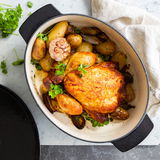 Gusseiserner ovaler Bräter mit gebratenem Hähnchen und Gemüse, von oben fotografiert.