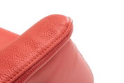 Close-up van een rode leren relaxfauteuil, met de nadruk op de armleuning, gezien vanuit de zijkant.