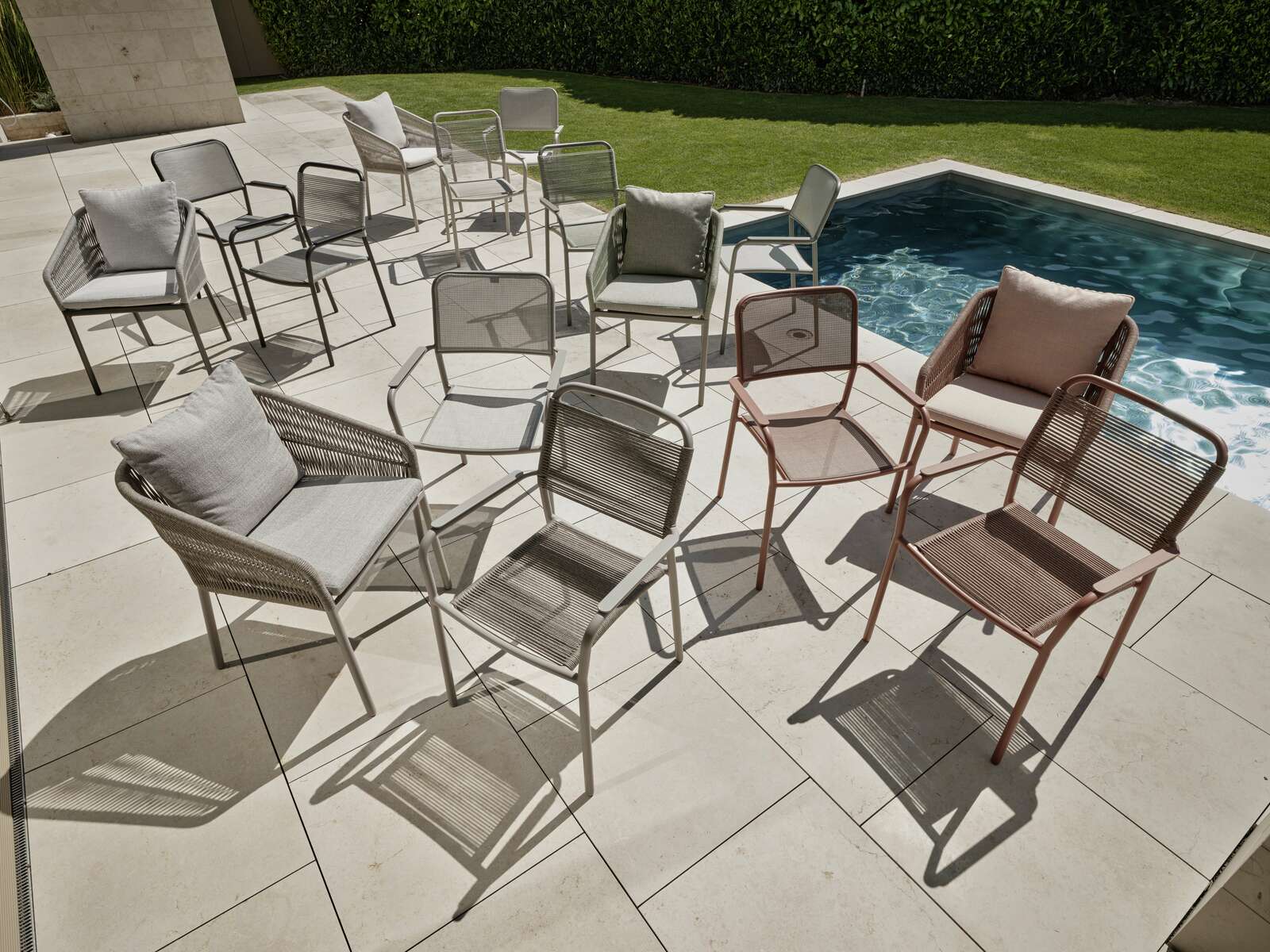 Mehrere Stapelsessel in verschiedenen Farben stehen auf einer Terrasse neben einem Pool, fotografiert aus der Vogelperspektive.