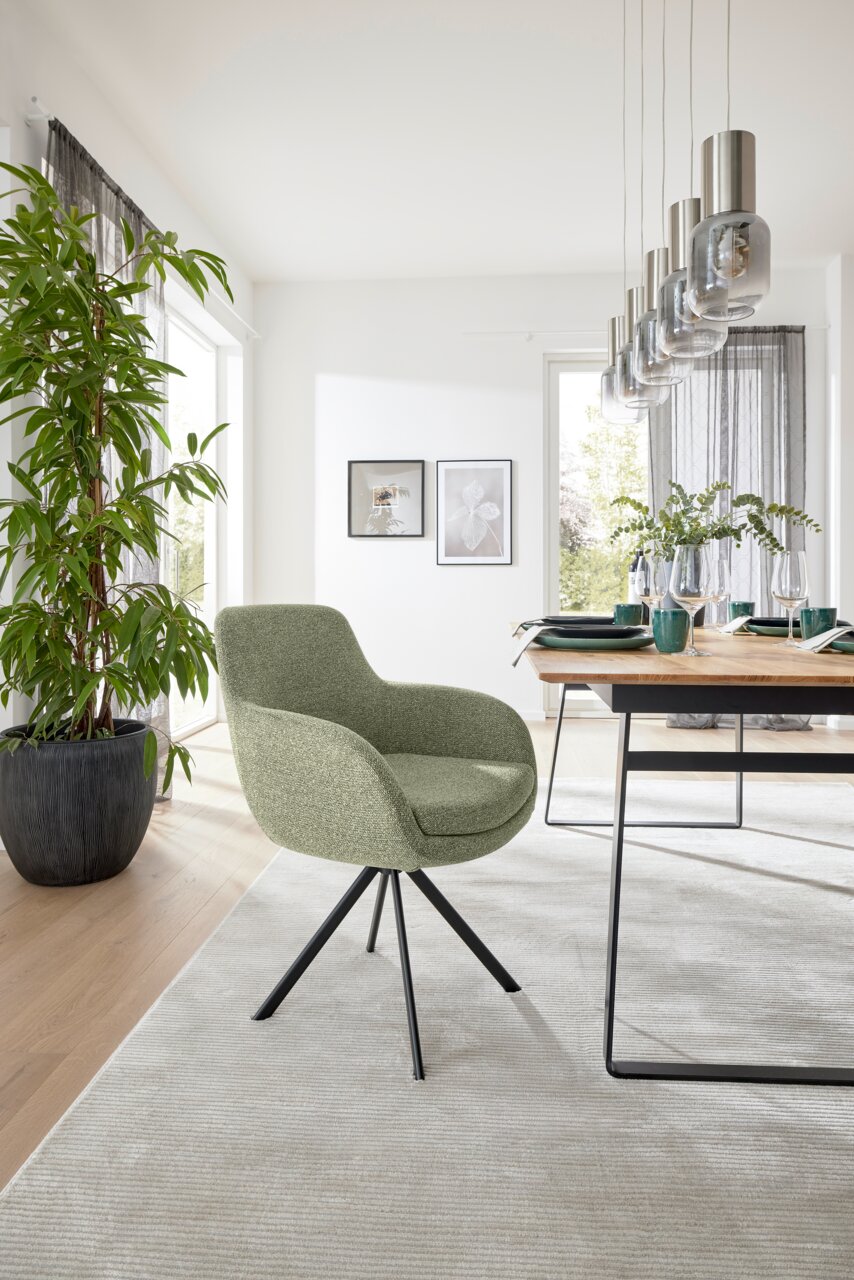 Grüner Armlehnstuhl mit schwarzem Metallgestell in einem modernen Esszimmer, seitliche Perspektive.