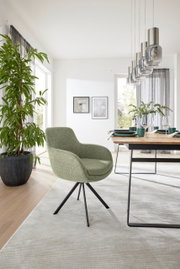 Grüner Armlehnstuhl mit schwarzem Metallgestell in einem modernen Esszimmer, seitliche Perspektive.
