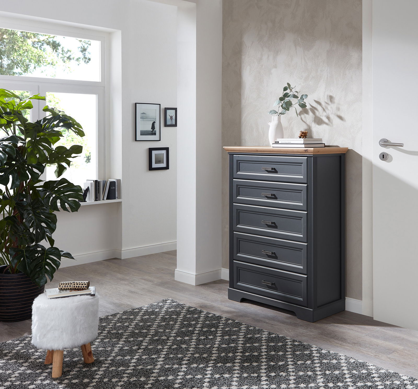 Schubkastenkommode in einem modernen Wohnzimmer, seitliche Perspektive, mit fünf Schubladen und einer Holzplatte, dekoriert mit einer Vase und Büchern.